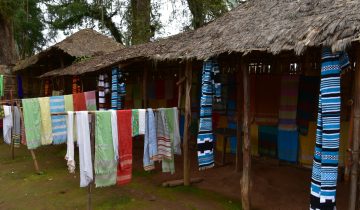 Handwoven striped cotton cloths made by Dorze weavers hang for sale outside thatched huts in southern Ethiopia, 2016