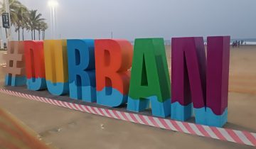 Large colorful letters spelling #DURBAN stand on the sand of the South Beach promenade in Durban, with palm trees and the sea behind, in 2025