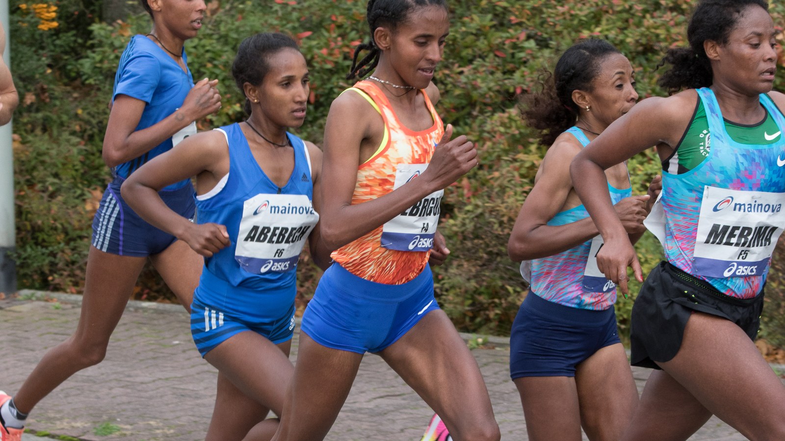 A group of Ethiopian women runners with race bibs reading Abebech, Yebrgual and Merima run on a road lined with autumn bushes at the 2017 Frankfurt Marathon