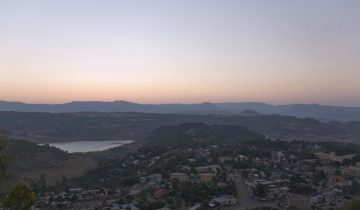 View from a hill over the houses and trees of Gondar, Ethiopia, with a lake and mountains under an orange evening sky in 2007