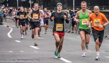 Amateur runners wearing yellow race numbers run along a Dublin road during the 2012 Dublin Marathon, with fans behind metal barriers