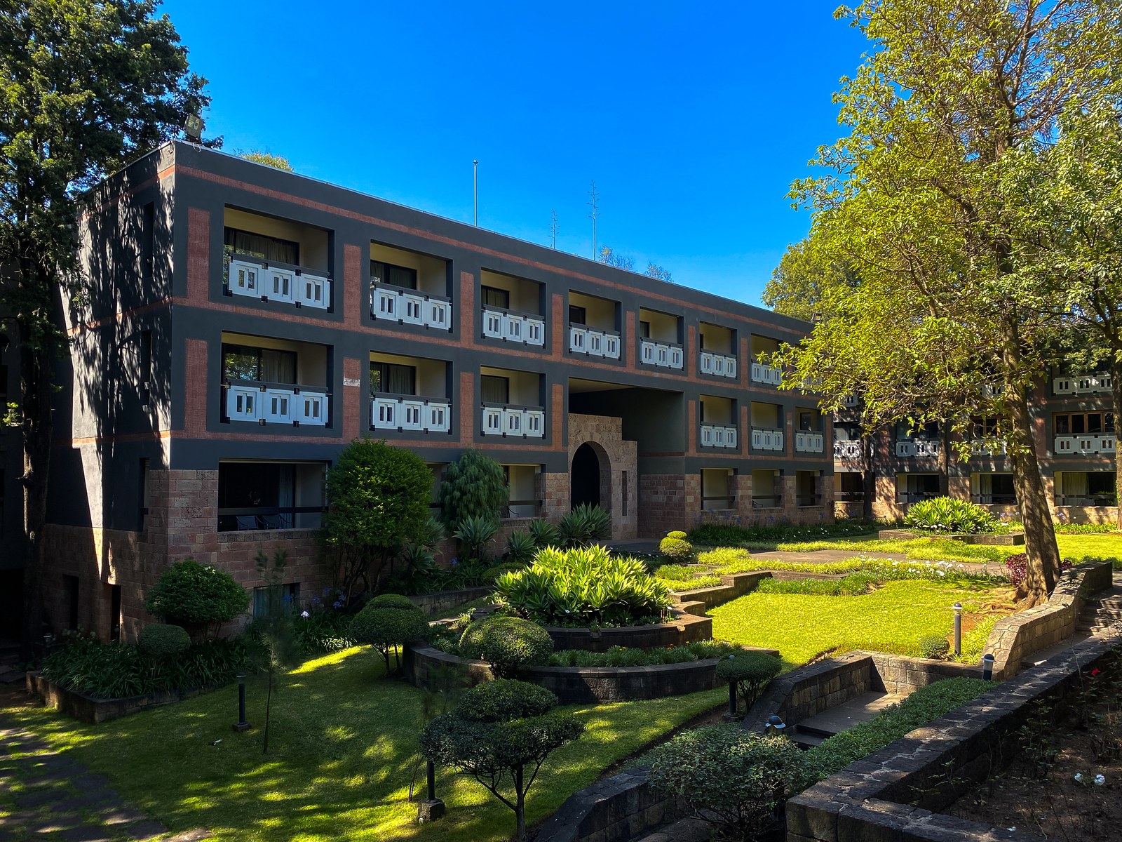 A four-story building with white balconies beside a green garden with trees at the Hilton Addis Ababa