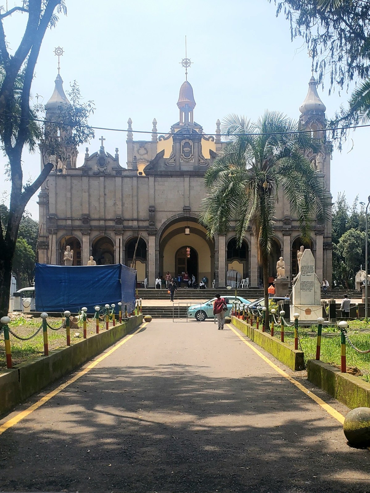 The front of Holy Trinity Cathedral in Addis Ababa, with domes and towers, seen at the end of a paved path lined with palm trees and grass in 2025